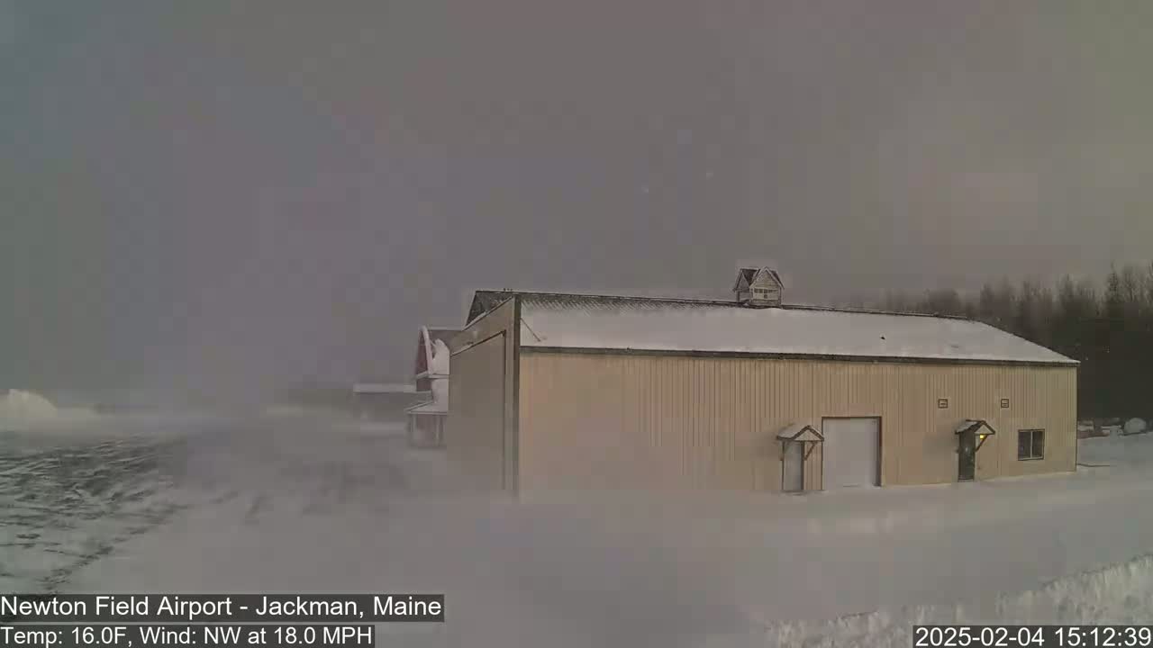 A tan building covered in snow is partially obscured by heavy snowfall and strong northwest winds.