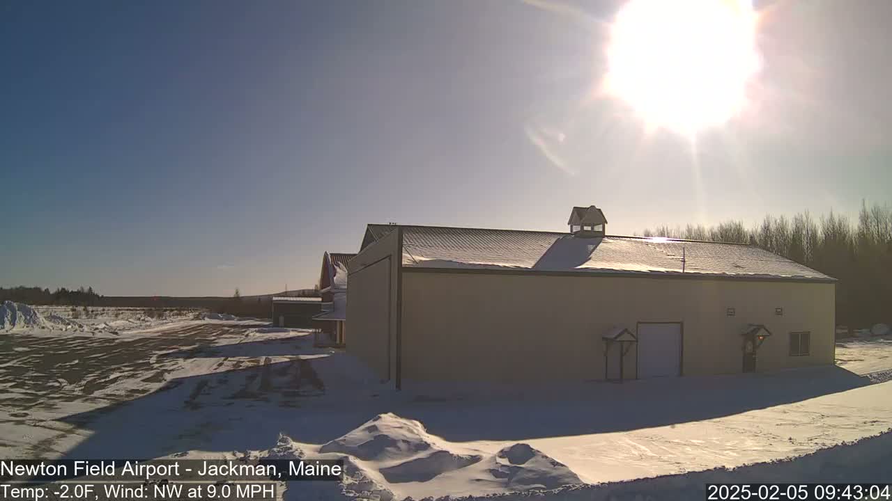 A snow-covered airfield with a large tan building under a bright, sunny sky.