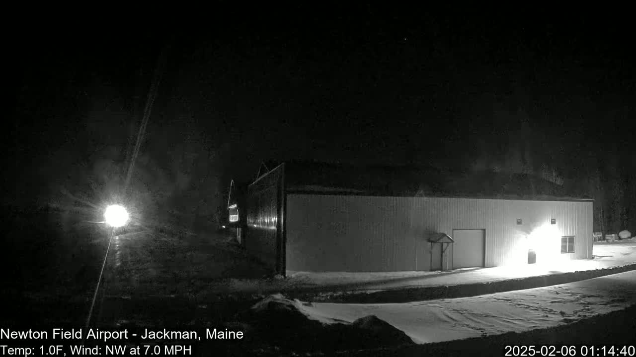 A long, low building is illuminated at night in snowy conditions under a dark sky.