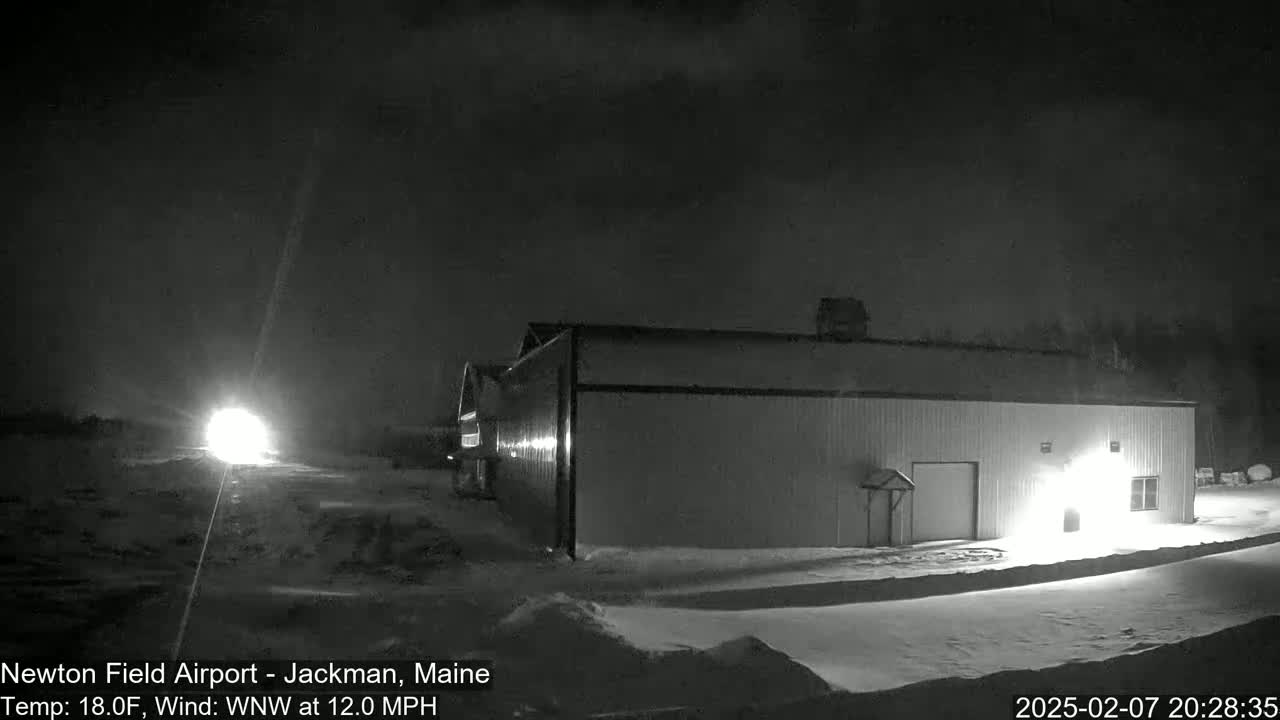 A long, low building is illuminated at night in snowy conditions with a wind of 12 mph from the west-northwest.