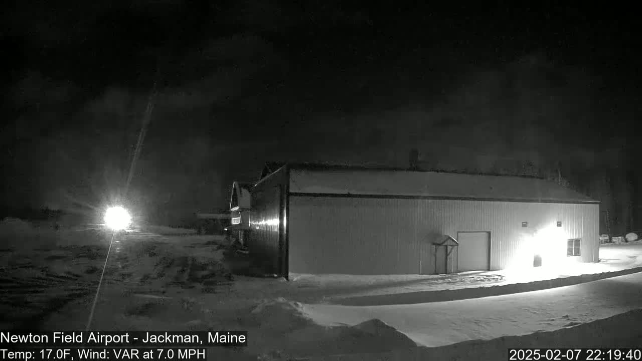 A large, single-story building is illuminated at night in snowy conditions under a dark, cloudy sky.