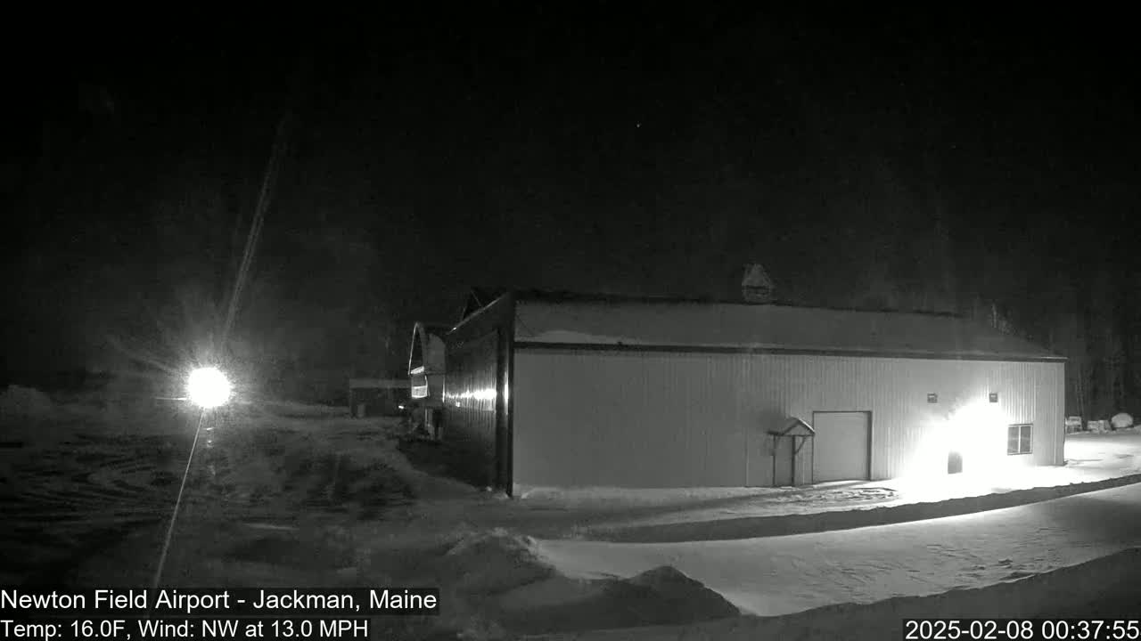 A large, light-colored building is illuminated at night in a snowy landscape under a dark sky with a northwest wind blowing at 13 mph.