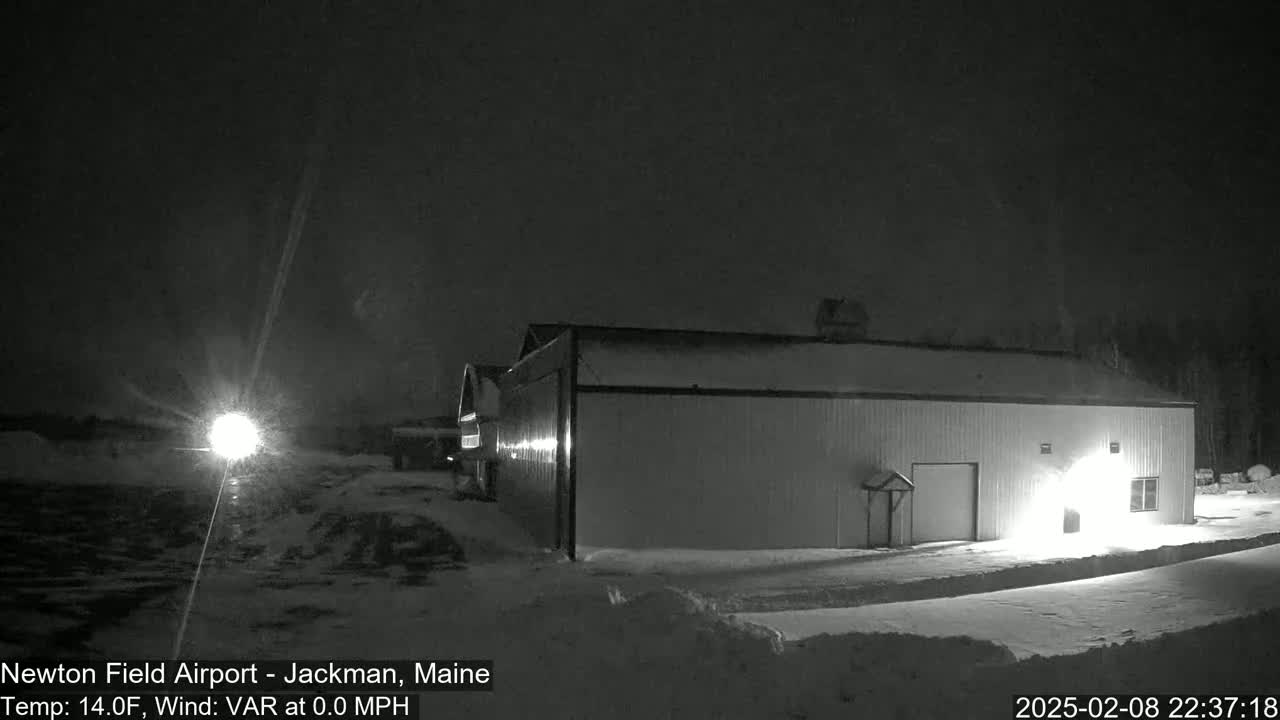 A long, light-colored building is illuminated at night in a snowy landscape under a dark sky.