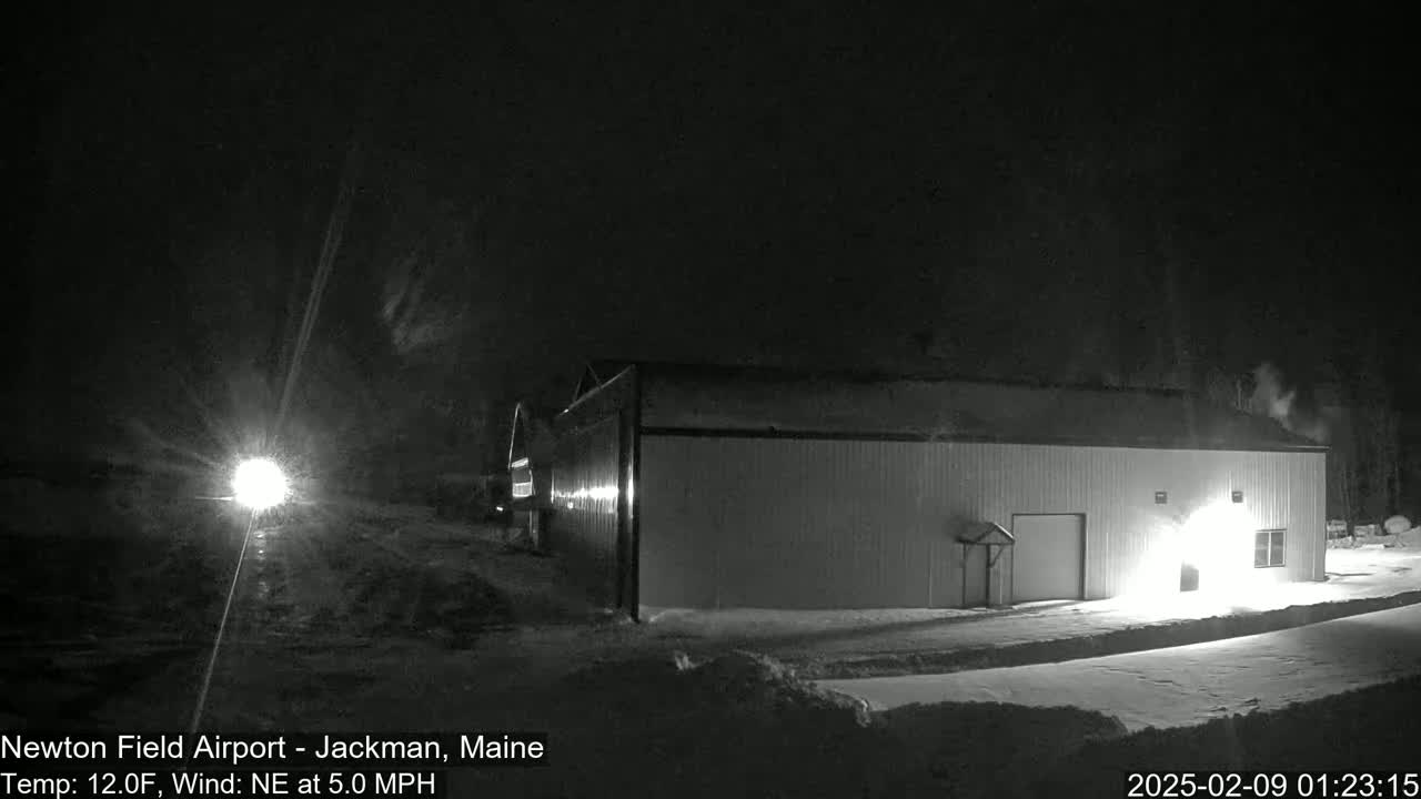 A long, white building is illuminated at night in snowy conditions with a northeast wind.