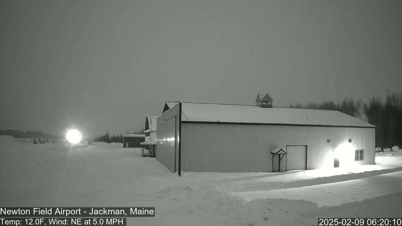 A large, light-colored hangar sits in a snow-covered landscape under a twilight sky with a northeast wind.