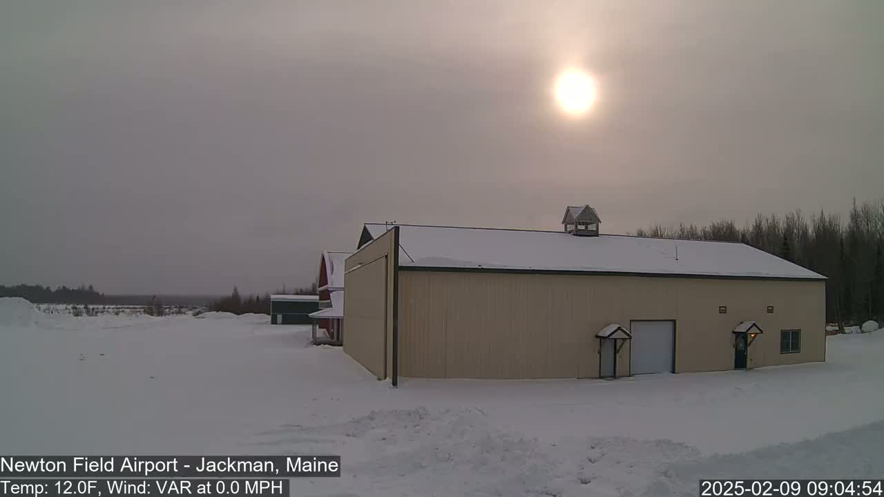 A tan hangar sits in a snow-covered landscape under a hazy sun.