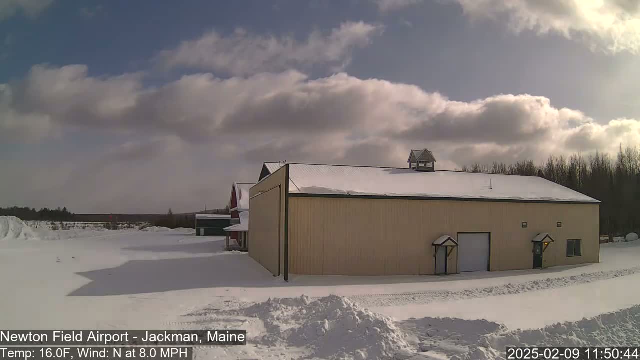 A tan hangar sits in a snowy landscape under a partly cloudy sky.