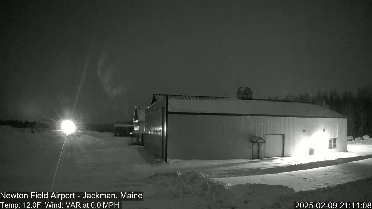 A large, snow-covered hangar sits in a snow-covered field at night under a dark sky.
