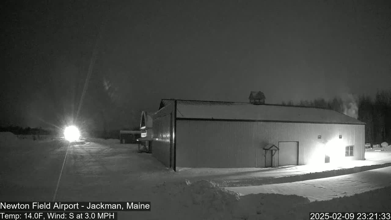 A large, light-colored hangar sits in a snow-covered area at night under a dark sky.