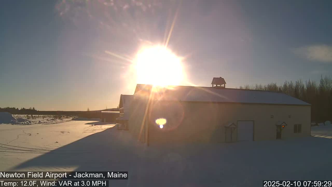 A snow-covered landscape with a large, light-colored building is brightly lit by a low winter sun.