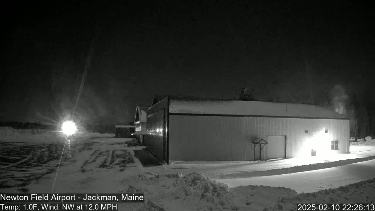 A large, snow-covered hangar is illuminated at night in a snowy landscape under a dark sky with a northwest wind at 12 mph and a temperature of 1°F.