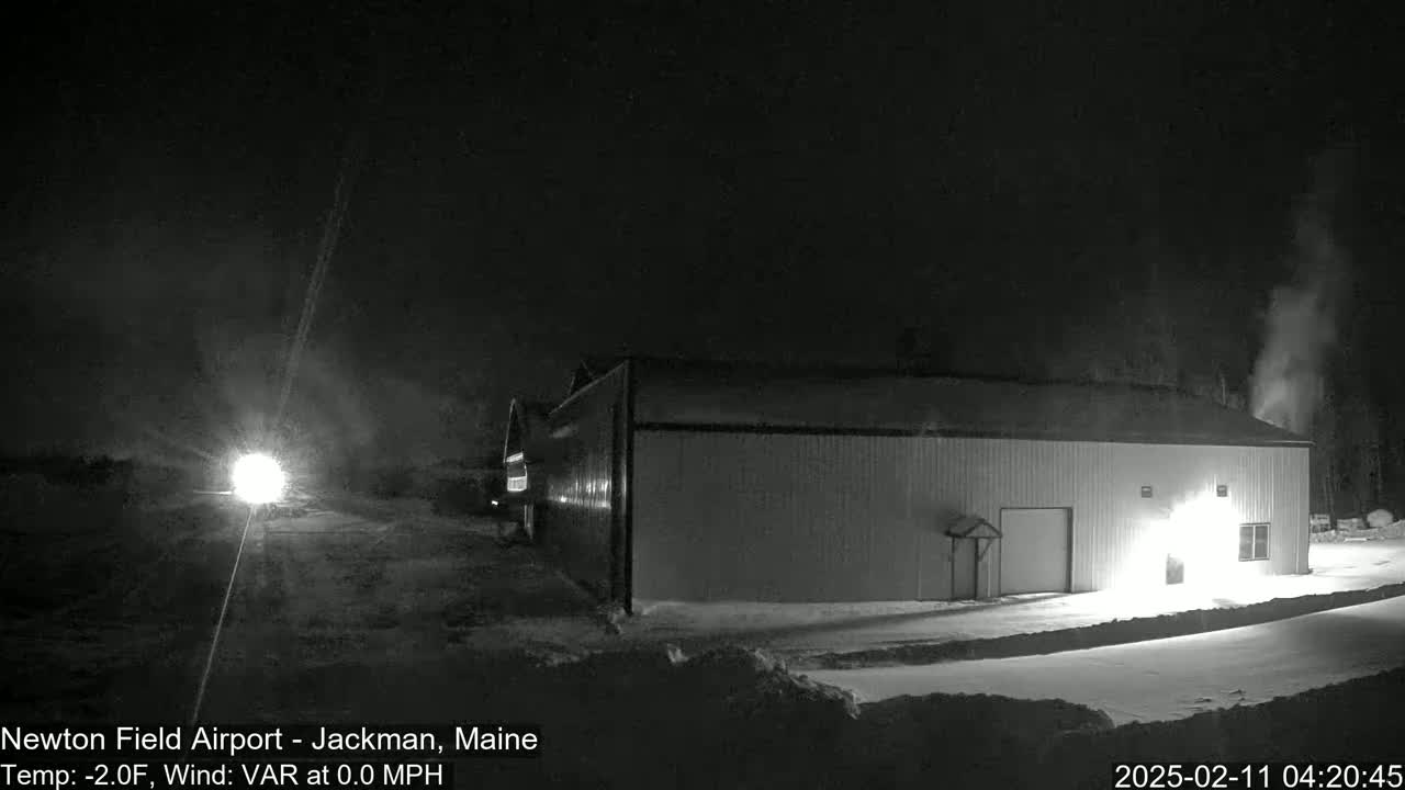 A long, low building is illuminated at night in a snowy area with calm, cold weather.
