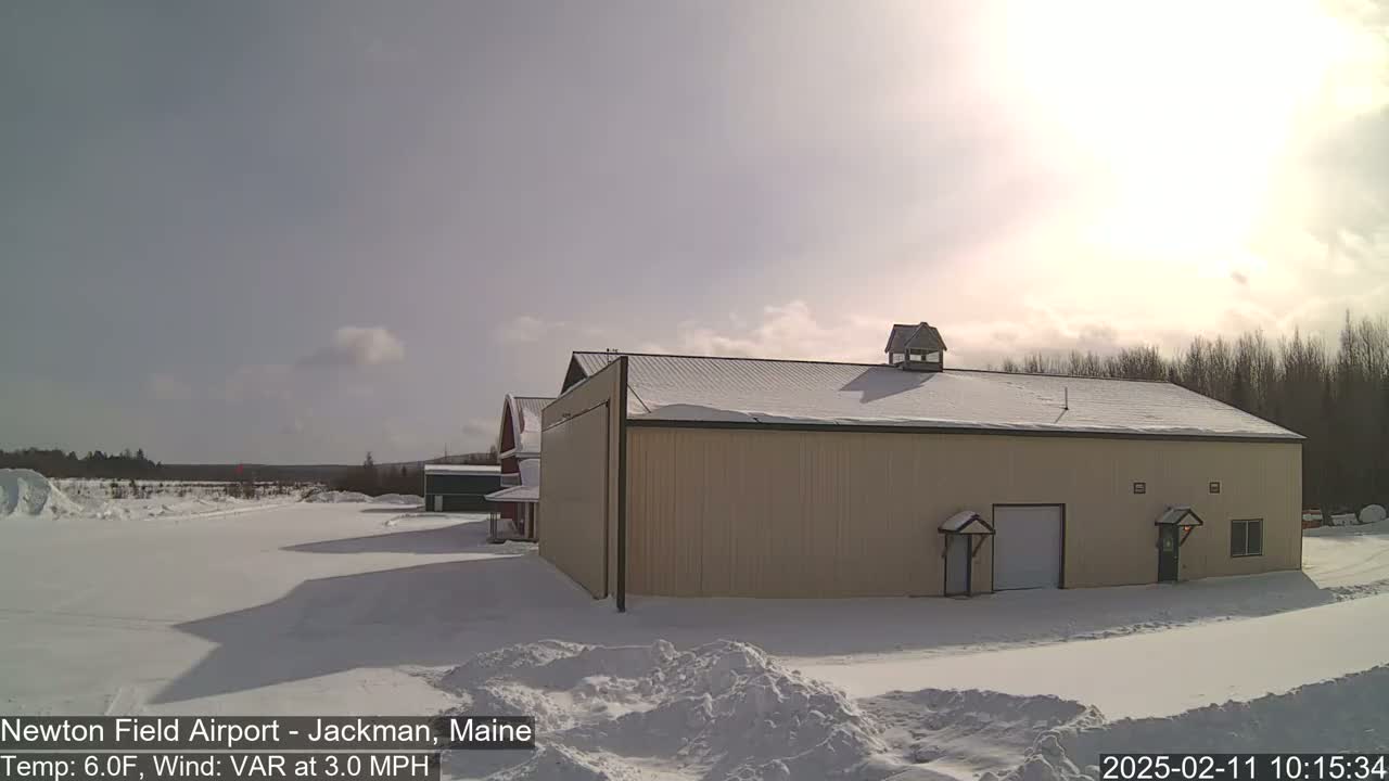A tan building with a snow-covered roof sits in a snowy landscape under a bright, sunny sky.