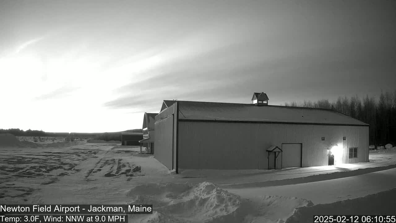 A large, single-story building sits in a snow-covered landscape under a twilight sky with a light wind.