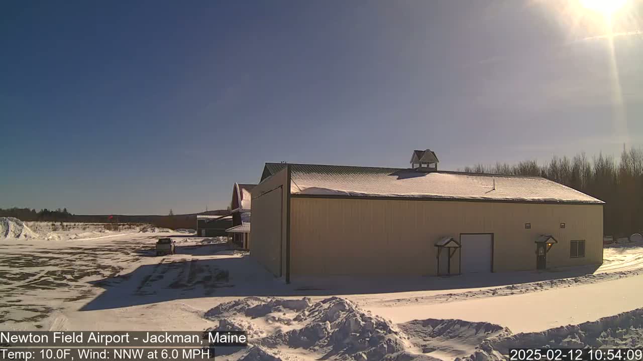 A large tan building with a snow-covered roof sits in a snowy landscape under a clear, sunny sky.