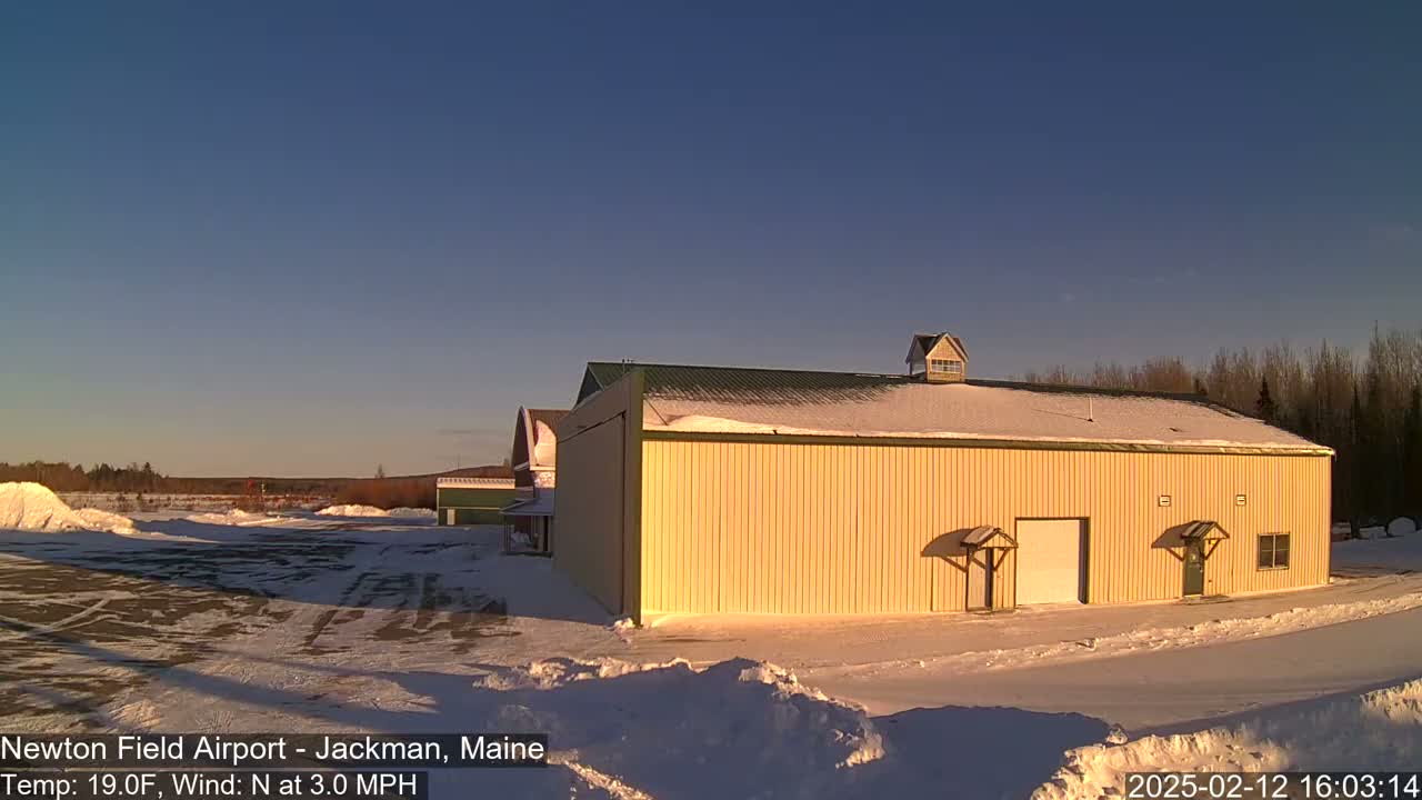 A large, pale-yellow building with a snow-covered roof stands in a snow-covered landscape under a clear, bright blue sky.