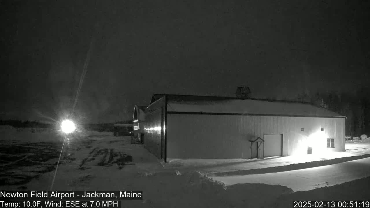A snow-covered hangar is illuminated at night under a dark sky with a 10°F temperature and a 7 mph ESE wind.