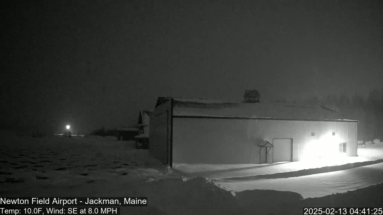A large, light-colored building is illuminated in a snowy landscape at night under a dark sky, with a slight southeast wind.