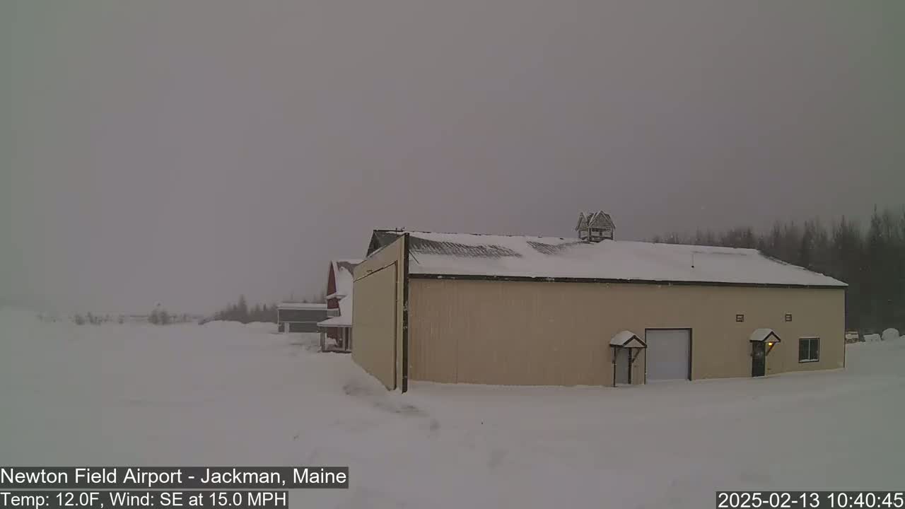 A large tan building with a snow-covered roof stands in a snowy landscape under an overcast sky, with a southeasterly wind blowing at 15 mph.
