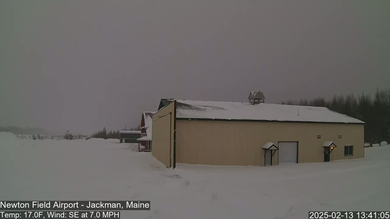 A tan building with a snow-covered roof sits in a snowy landscape under an overcast sky.