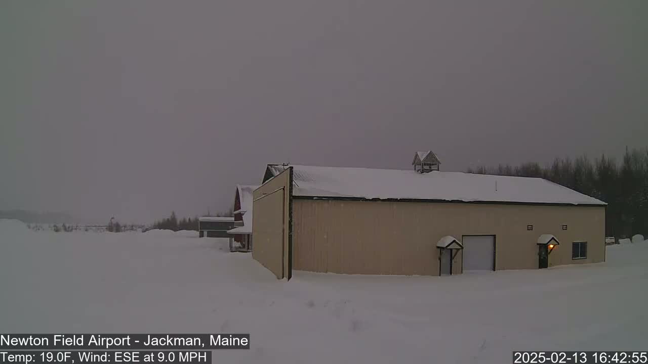 A tan building with a snow-covered roof sits in a snowy landscape under an overcast sky.