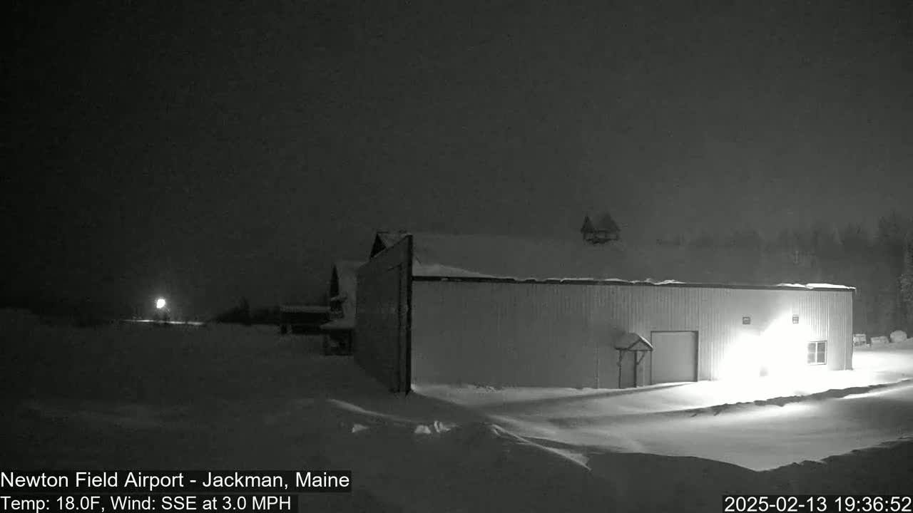 A snow-covered building is illuminated at night under a dark sky with a light wind.