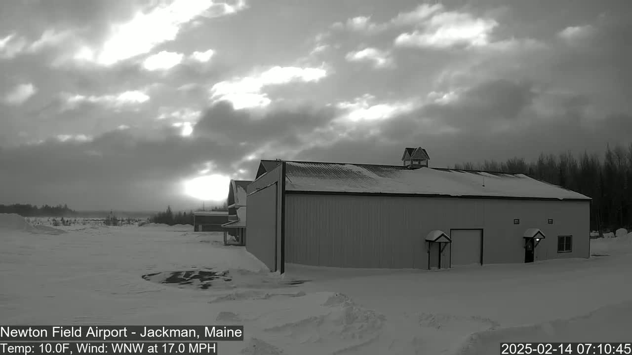 A large, snow-covered building stands in a snowy landscape under a cloudy sky, with a faint sunrise visible in the distance.