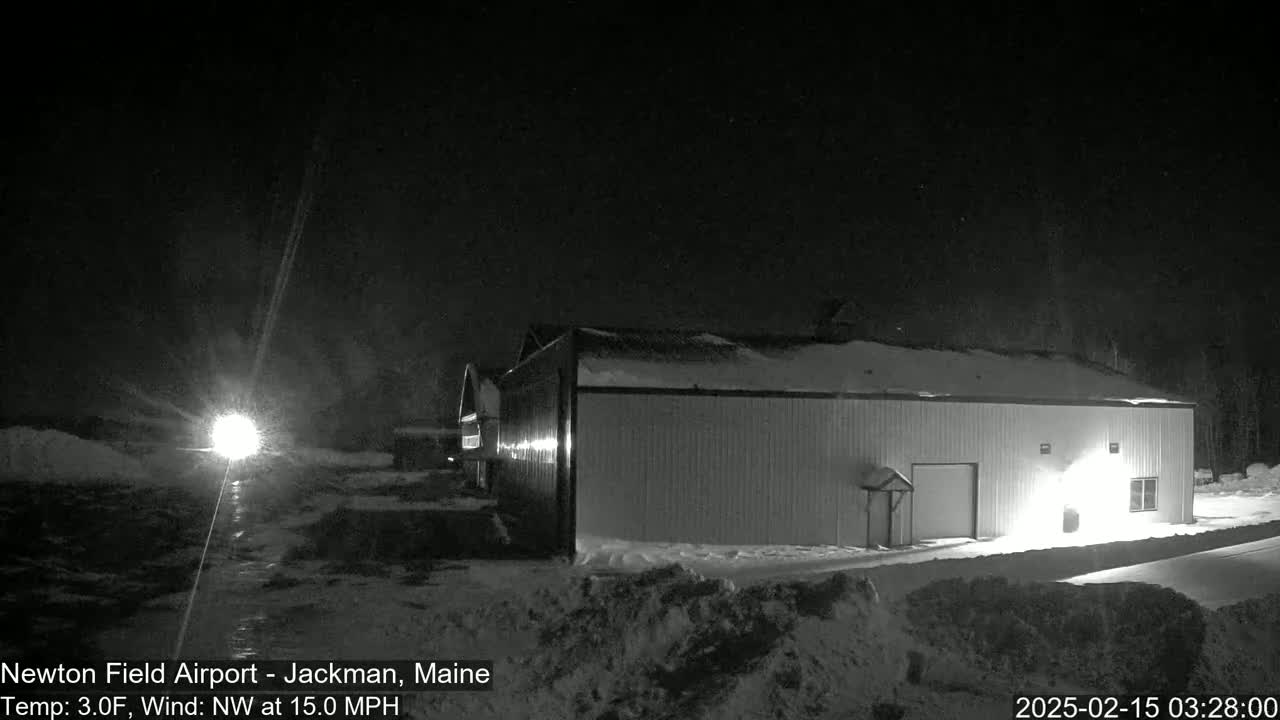 A long, light-colored building is illuminated at night in a snowy landscape under a dark sky with a northwest wind.