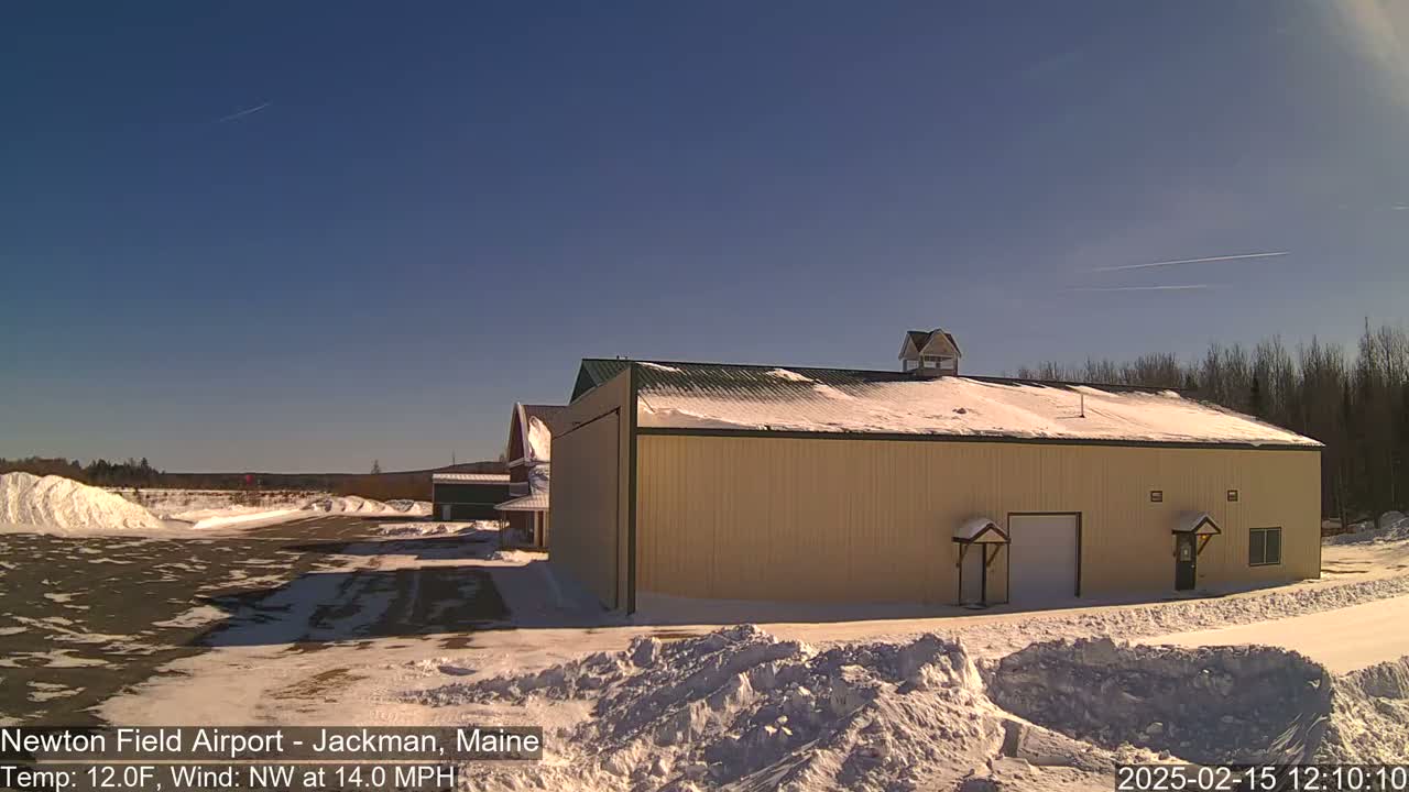 A large tan hangar sits on a snowy airfield under a clear blue sky.