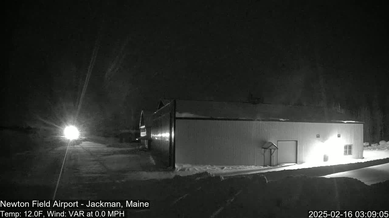 A snow-covered hangar is illuminated at night under a dark, possibly snowy sky.