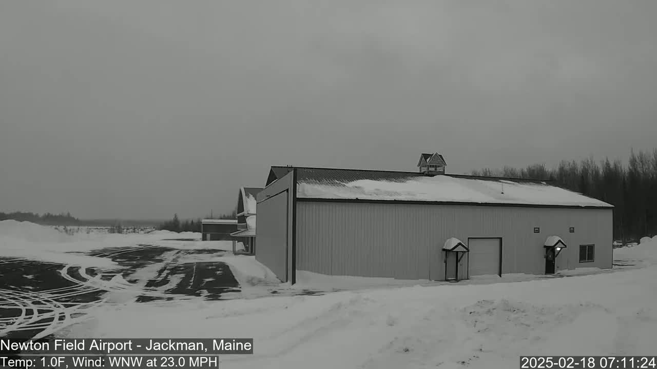 A large hangar sits in a snowy landscape under an overcast sky, with a smaller building visible in the background.