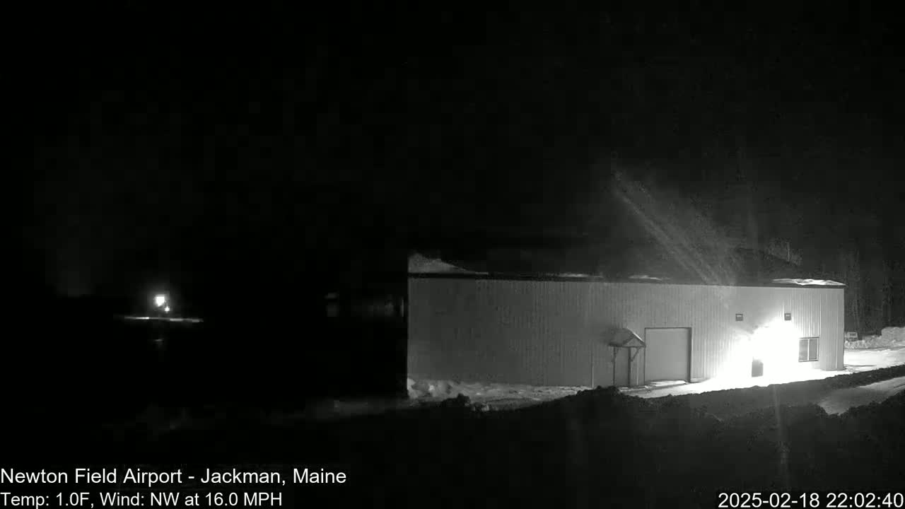 A long, low building is illuminated at night in snowy conditions with a northwest wind blowing at 16 mph.