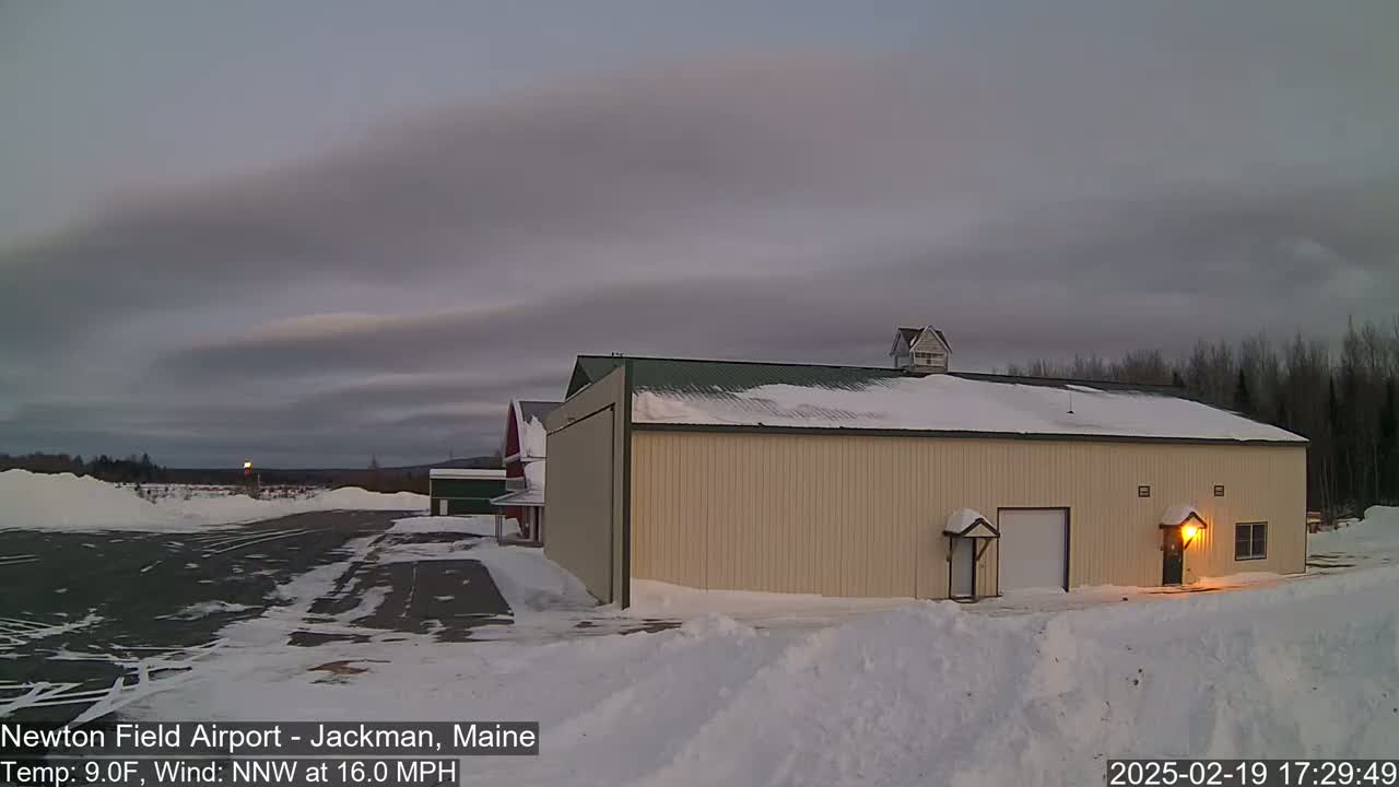 A tan hangar sits on a snow-covered airfield under a cloudy, twilight sky.