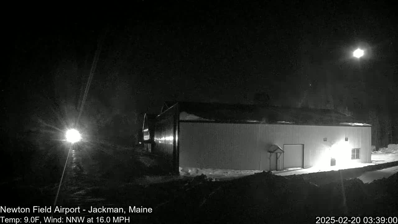 A brightly lit building stands in a snowy landscape under a night sky with a bright moon and a northwest wind blowing at 16 mph.