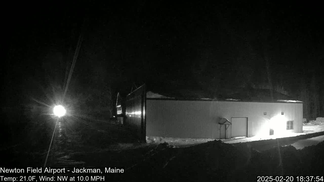 A long, light-colored building is illuminated at night in snowy conditions with a northwest wind.