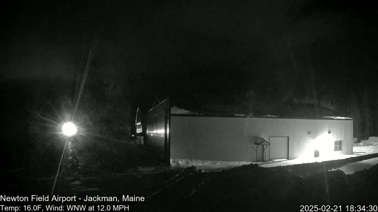 A bright light shines from a vehicle in front of a long, white building under a dark, clear night sky.