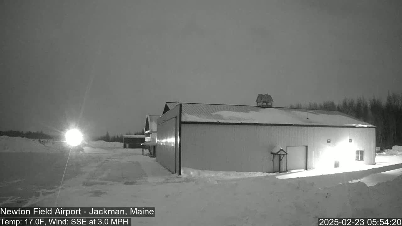 A large, snow-covered hangar sits in a snowy, dimly lit airfield under a dark, overcast sky.