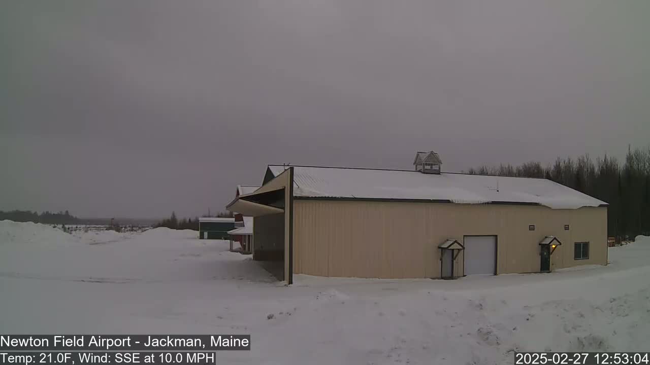 A large tan building with a snow-covered roof sits in a snow-covered landscape under an overcast sky.