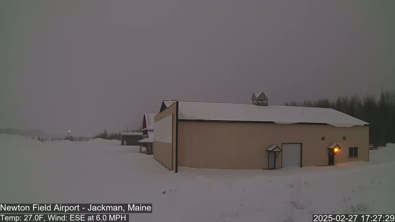 A tan building with a snow-covered roof stands in a snowy landscape under a gray sky.