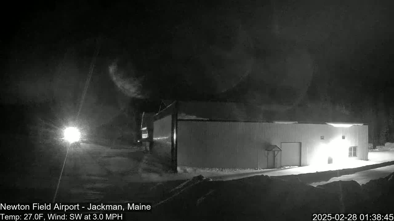 A long, white building is illuminated at night in snowy conditions with a southwest wind.
