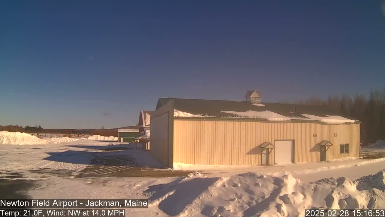 A large, tan building with a snow-covered roof stands in a snowy landscape under a clear blue sky.