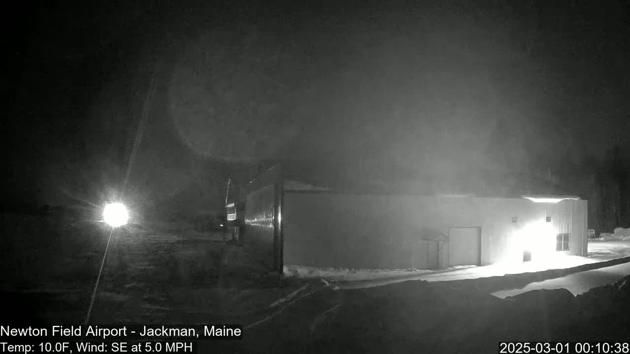 A light-colored building is illuminated at night in snowy conditions with a southeast wind.