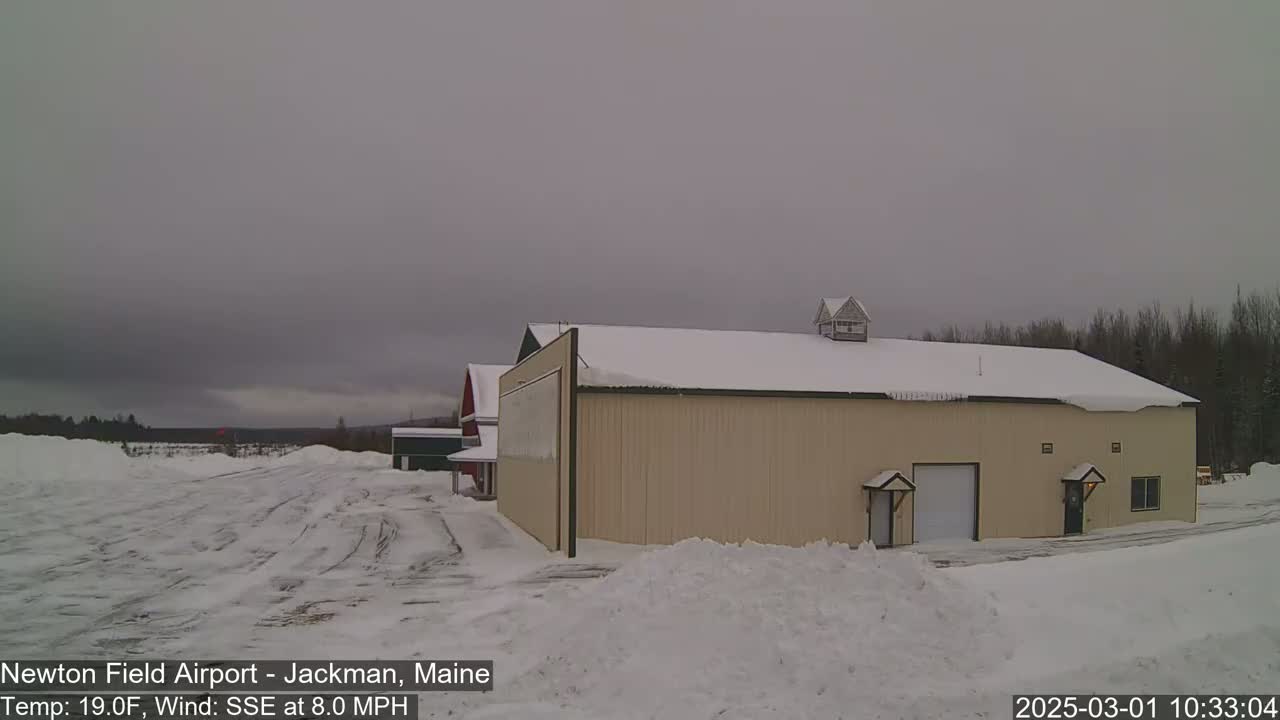 A tan hangar sits in a snow-covered airfield under an overcast sky, with a gentle wind blowing from the south-southeast.