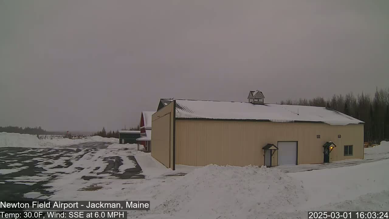 A tan hangar sits in a snowy airfield under an overcast sky.