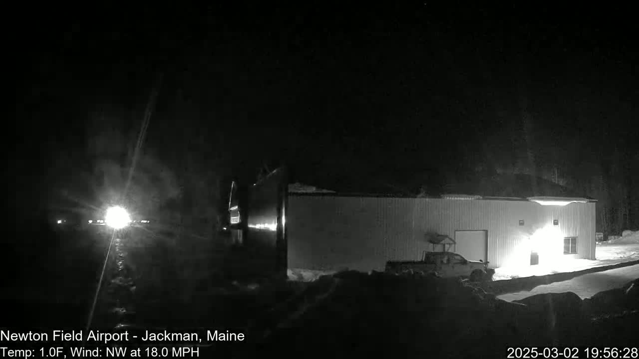 A long, low building is illuminated at night under a dark sky with a northwest wind of 18 mph and a temperature of 1 degree Fahrenheit.