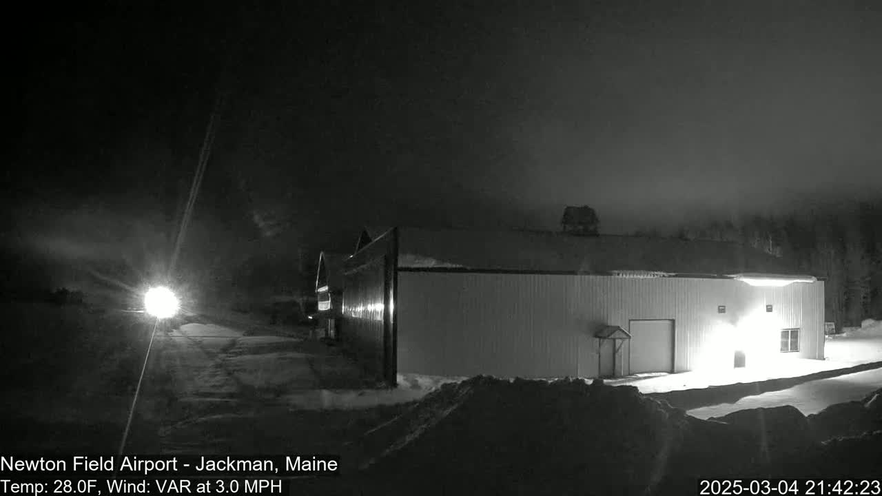 A long, low building is illuminated at night in snowy conditions under a dark, mostly clear sky.