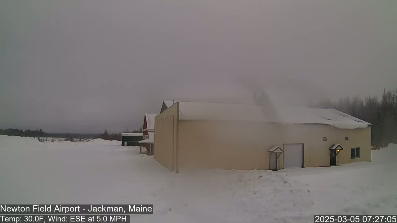 A tan building with a snow-covered roof stands in a snowy landscape under a hazy, overcast sky.