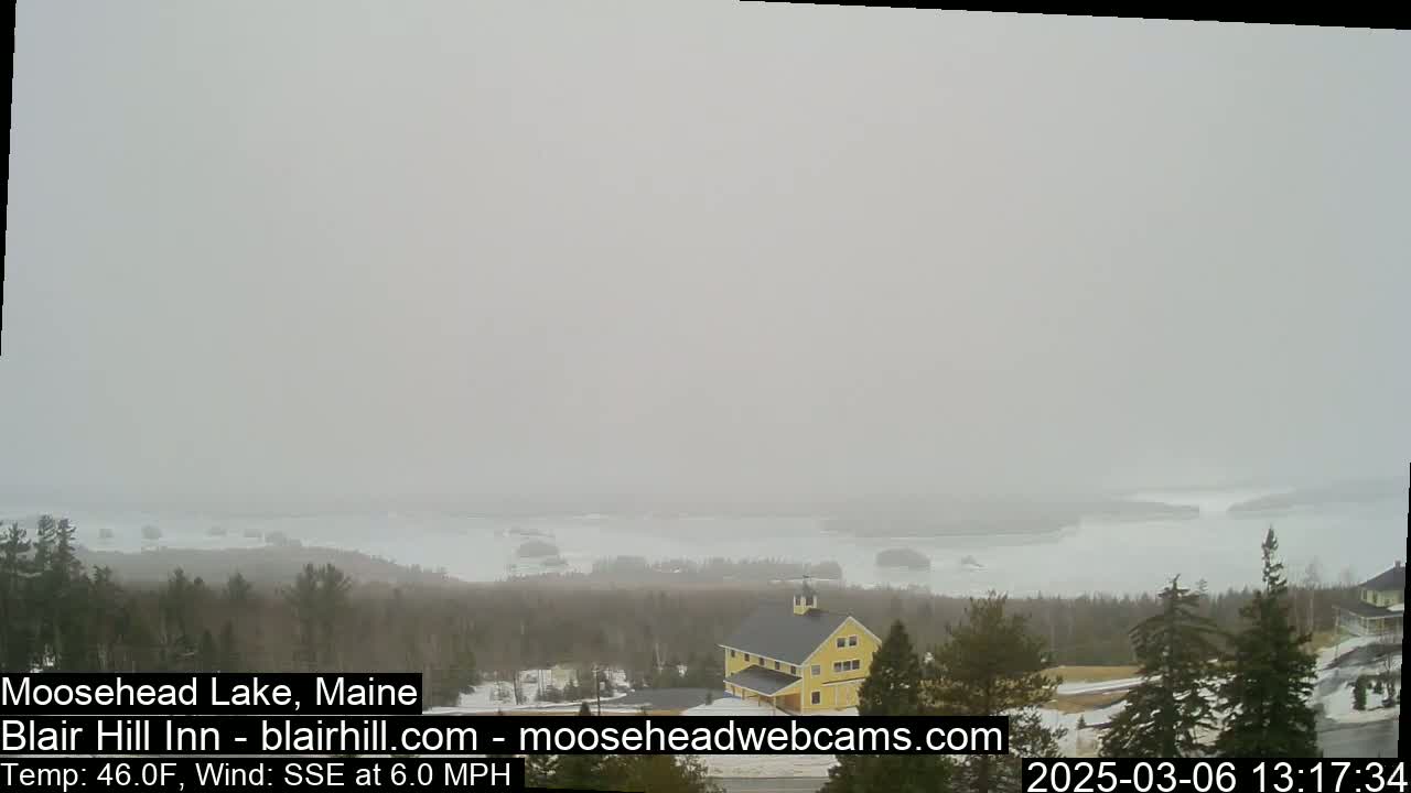 A hazy, snowy view of a lake and distant islands with a yellow building and trees in the foreground.