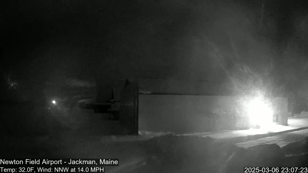 A snowstorm at night illuminates a building with bright lights,  with a strong wind blowing snow.