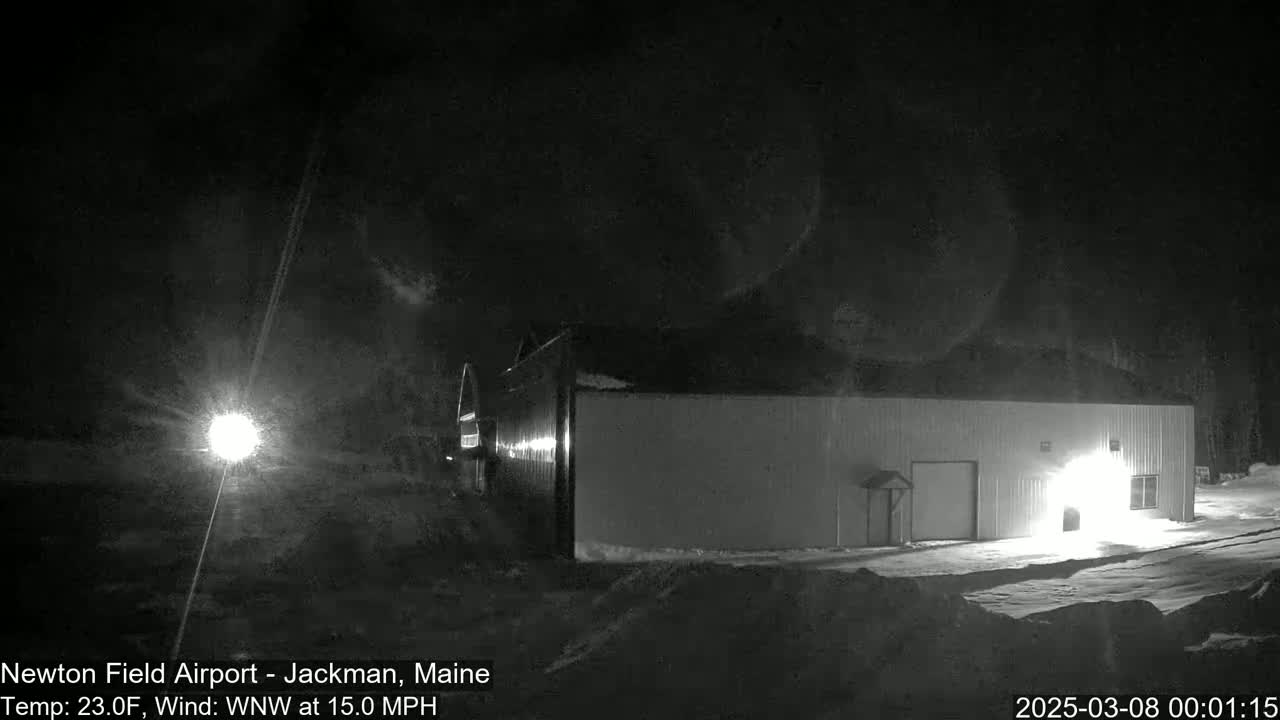 A large, light-colored building is illuminated at night in snowy conditions with a 15 mph wind.